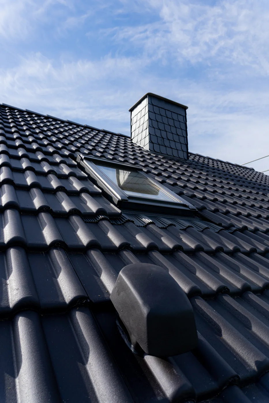 Dachfenster und schieferbekleideter Kamin auf einem neu eingedeckten Dach